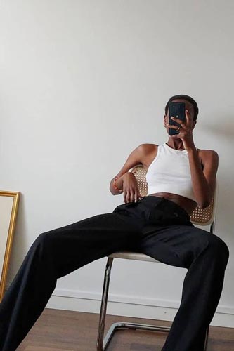 model sitting on metal chair wearing white tank top and black trousers