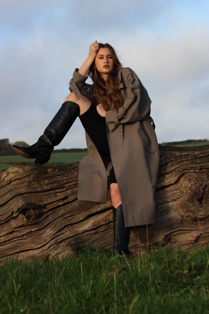 Winter 2022 Boot Trends -leather cowboy boots - woman sitting on the pal wearing black leather boots and trench coat