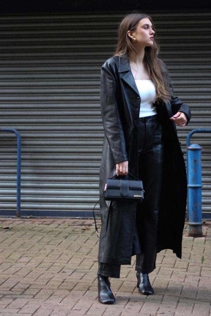 woman wearing long black leather coat paired with black Jacquemus logo bag and leather pants